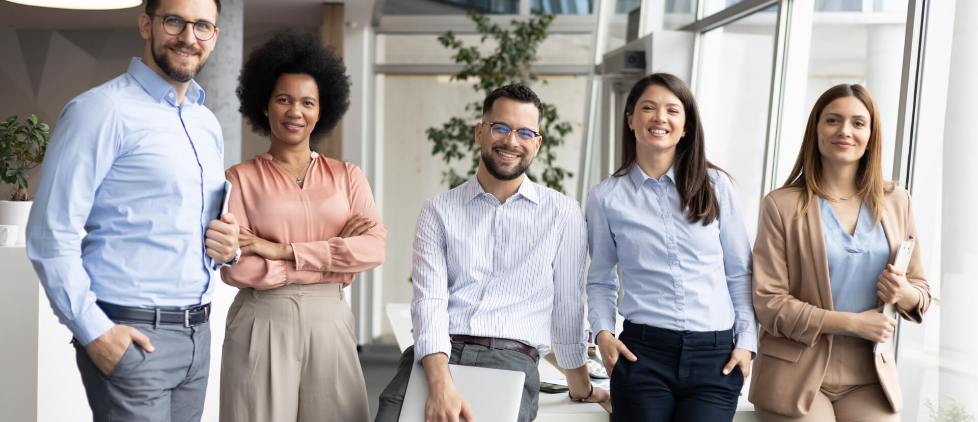 Five smiling colleagues standing together in a bright, modern office
