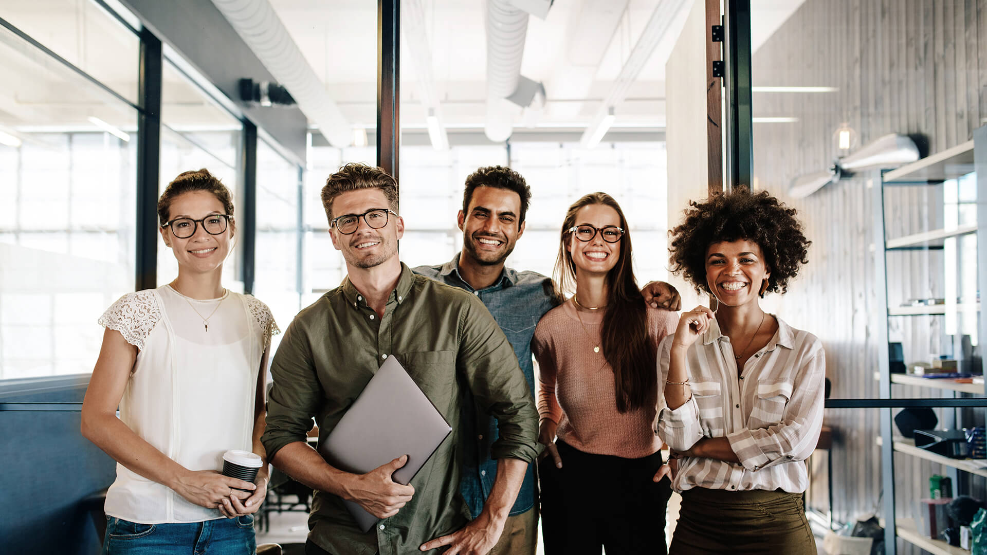 Cheerful team of five standing together, laughing, in a modern loft office