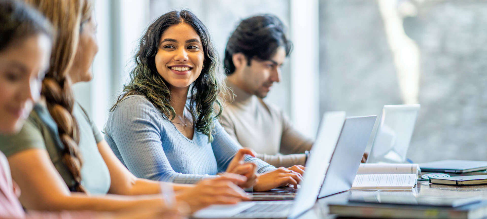 Smiling student employee at a laptop, colleagues working beside her at a table