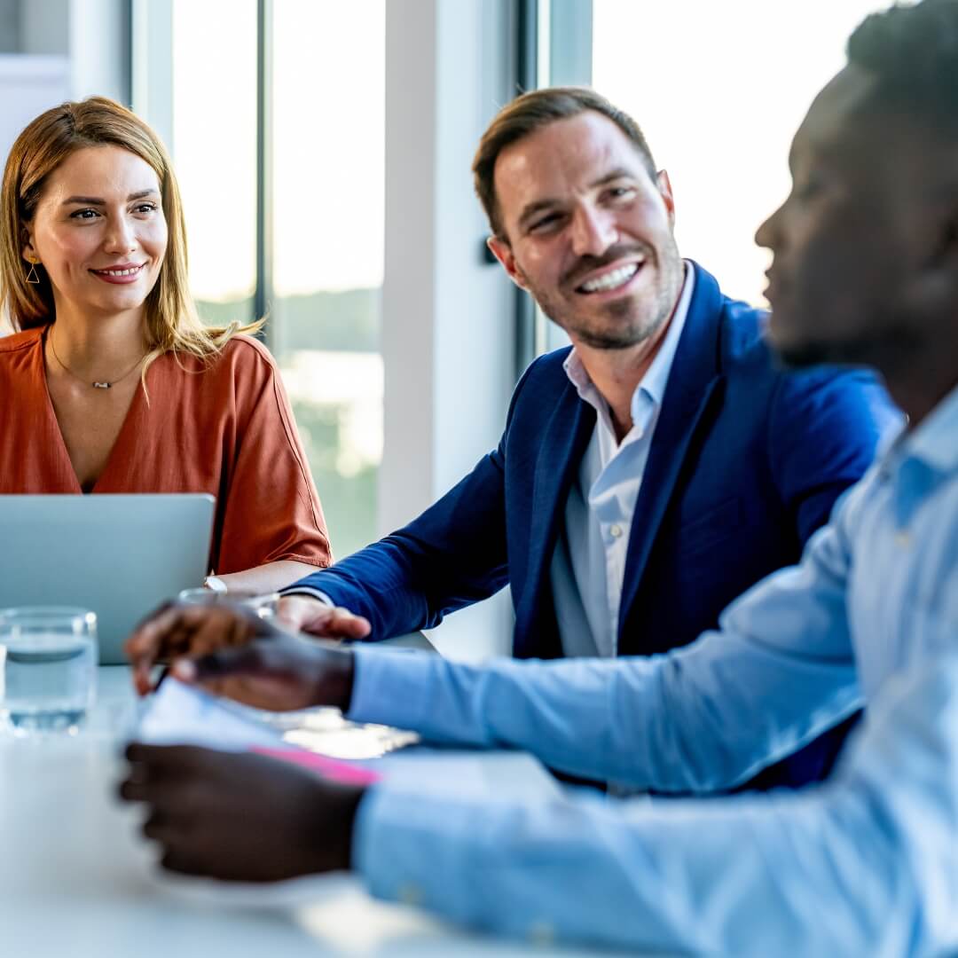 A woman and two men chatting and smiling in a bright meeting room