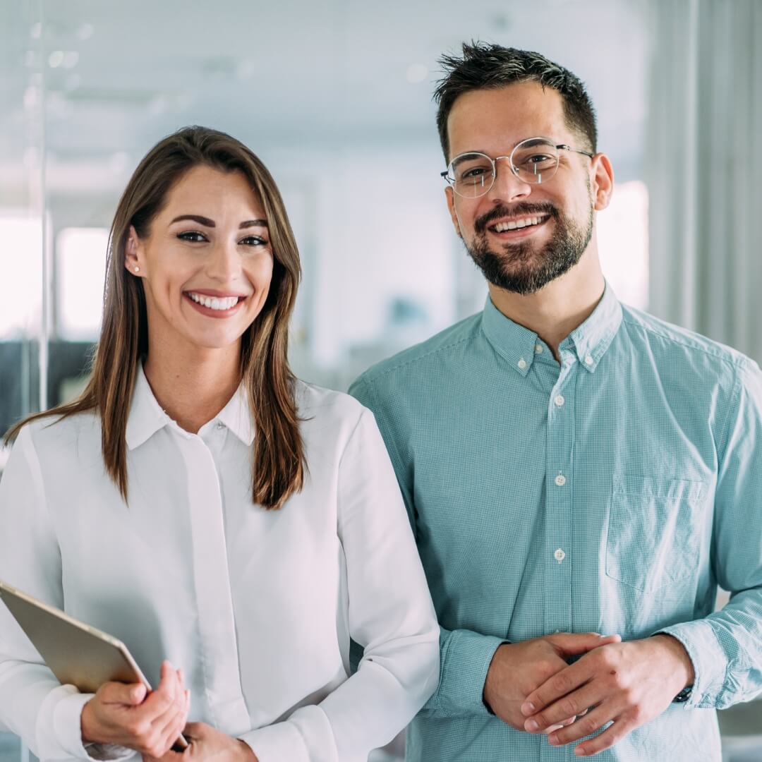 Female colleague with a tablet and male colleague with glasses smiling in an office