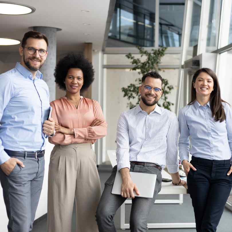 Vier lächelnde Kolleginnen und Kollegen stehen gemeinsam in einem hellen, modernen Büro